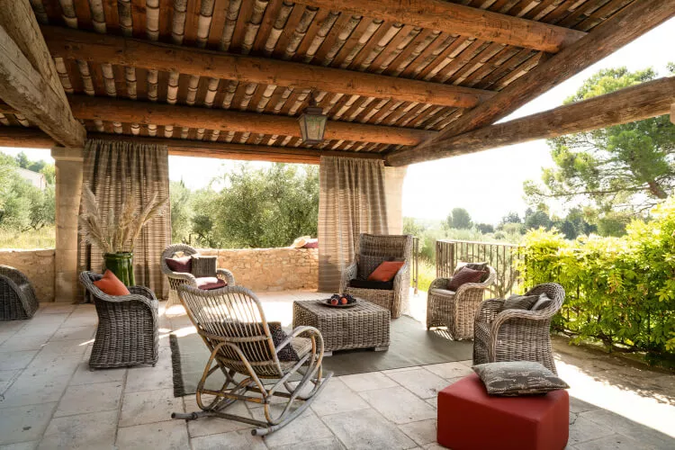 Eine sonnige Terrasse im Landhaus-Stil mit braun-beige gestreiften Vorhängen, einem Schaukelstuhl und Rattanmöbeln.