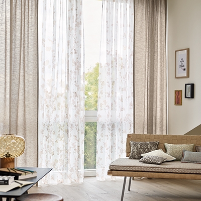 Klassische Fensterdekoration mit zweiläufiger Gardinenschiene, weißem, transparentem Voile mit beigem Blattmuster und passenden beigen Vorhängen.