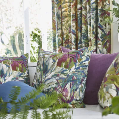 Eine Detailaufnahme von sehr farbenfrohen Kissen und einem Vorhang mit Pflanzenmotiven in einem Wohnzimmer.