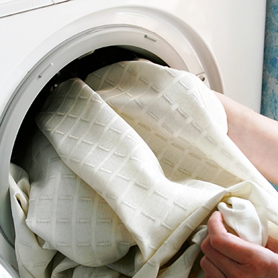 Ein elfenbeinfarbener Vorhang wird aus der Waschmaschine geholt.