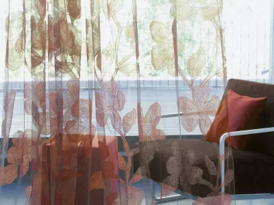Transparenter weinroter Tüllstoff mit kunstvollen Blumen, im Hintergrund eine Terrasse und ein Sessel