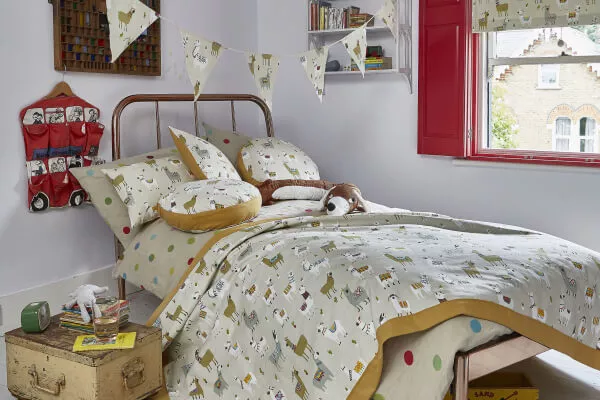 Ein Kinderzimmer mit Raffrollo, Tagesdecke, Kissen und Dekoration aus Baumwolle mit Lama-Motiv.