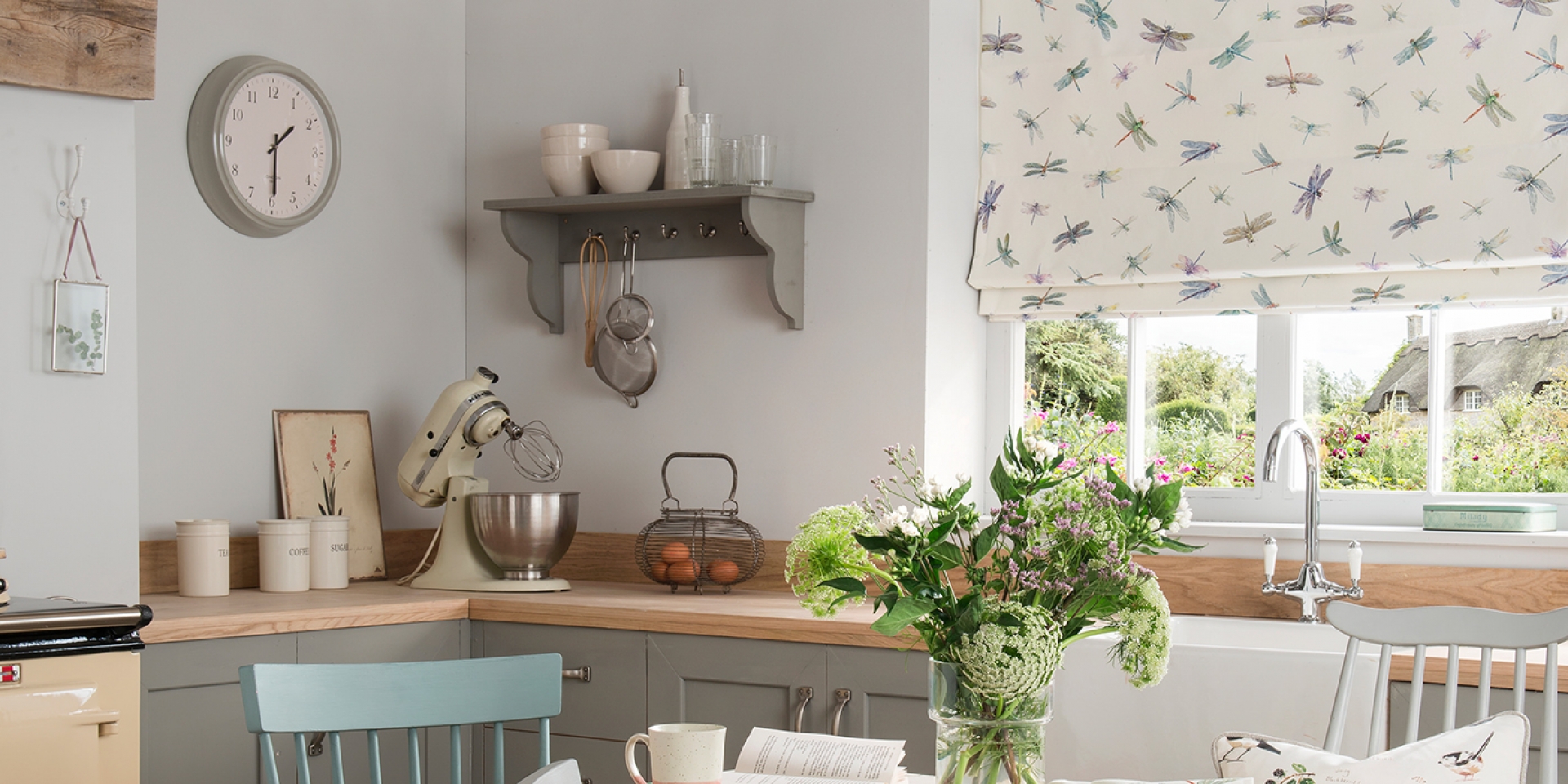 Küchenfenster mit weißem Raffrollo, verziert mit blauen, violetten, grünen und orangen Libellen-Muster.