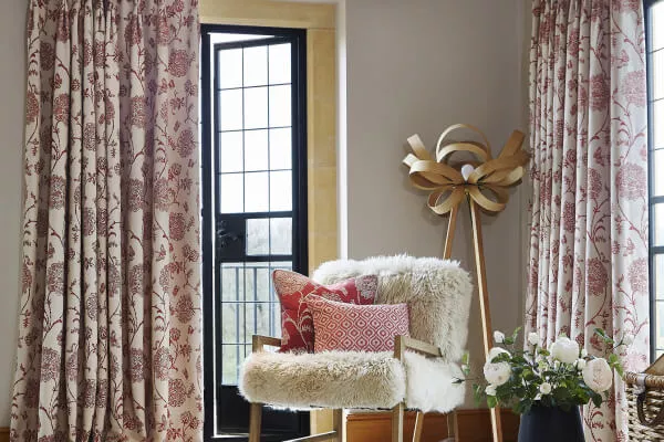 Faltenband-Vorhänge mit beige-rotem Blumenmuster im Landhausstil hängen in einem gemütlichen Wohnzimmer.