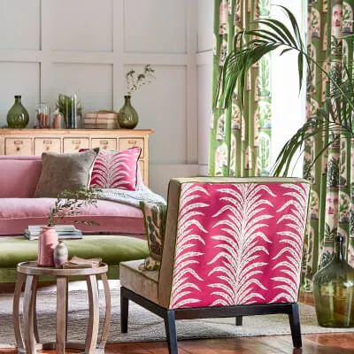 Ein bunt eingerichtetes Wohnzimmer mit Motivvorhängen und Couch sowie Sessel und grünen Pflanzen