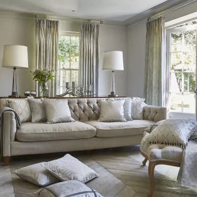 Transparente Vorhänge mit Faltenband hängen an einer Gardinenstange hinter einem Leinensofa im strengen klassischen Stil in einem Wohnzimmer.