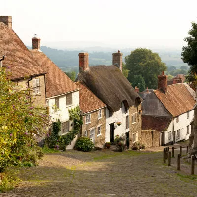 Mehrere charmante Landhäuser mit Strohdach im britischen Stil stehen an einer kleinen Straße.