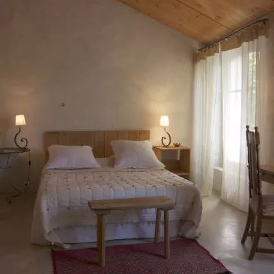 Ein gemütliches Schlafzimmer im Landhausstil mit einer weissen Tagesdecke und transparenten weissen Gardinen.