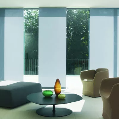 Glasfensterfront mit Flächenvorhang-Paneelen in Weiß-Grau und modernem Mobiliar davor.