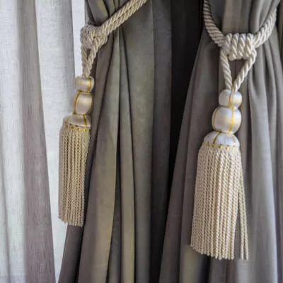 Eine Detailaufnahme eines Vorhangs mit klassischem Raffhalter in den Farben Beige, Grau und Gold.