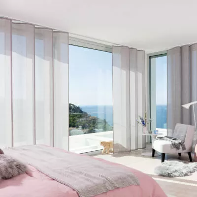 Schlafzimmer mit rosafarbenen überlappenden Schiebevorhängen, Sessel und Meerblick.