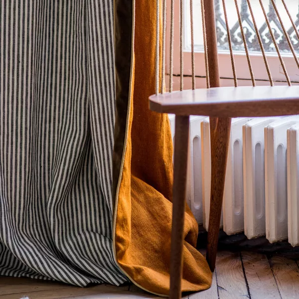 Leinenvorhang mit Streifenmuster und orange Hinterfütterung neben Fenster und Stuhl