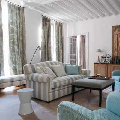 Ein gemütliches Wohnzimmer im Landhausstil mit mint-braunen Vorhängen und einem weiss-grün-blau gestreiften Sofa.