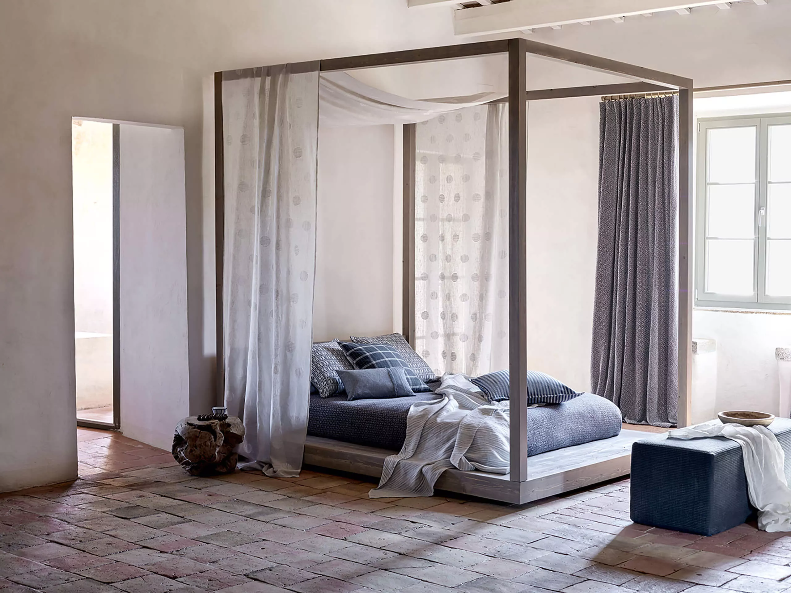 Schlafzimmer mit bodenlangen Baumwollgardinen und Himmelbett in blaugrauer sowie brauner Farbgebung