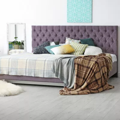 Ein großes Bett mit einem lila gepolsterten Kopfteil mit karierten Decken und verschiedenen bunten Kissen.