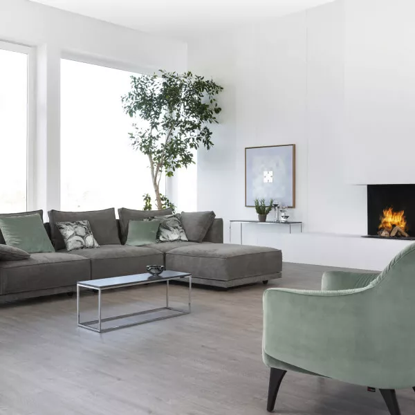 Wohnzimmer mit Couch und Sesseln sowie grauen transparenten Gardinen.