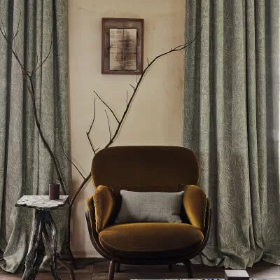 Graue Vorhänge mit Muster an einer Wand mit Sessel, der mit Samt bezogen ist.