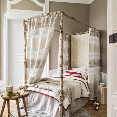 Ein Himmelbett aus Birkenästen in einem Schlafzimmer im Landhausstil mit beige gemusterten Vorhängen aus Leinen.