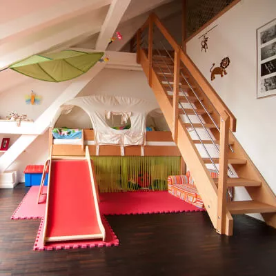Ein fröhlich buntes Kinderzimmer mit einer Rutsche, einem Schlafzelt und einem grünen Segel.