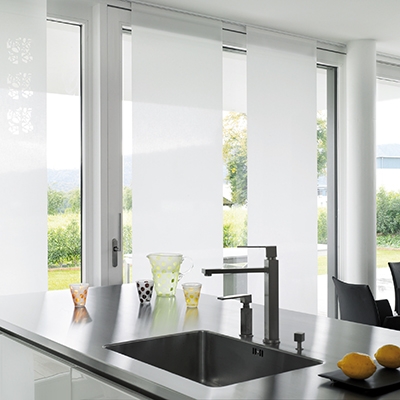 Moderne Küche mit verschiebbaren, halbtransparenten weißen Paneelen vor einer großen Fensterfront.