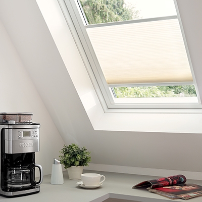Küchenfenster in Dachschräge mit cremefarbenem Plissee über einer Arbeitsfläche mit Kaffeemaschine und Tasse
