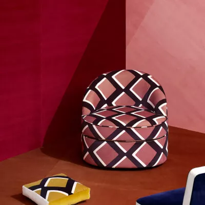 Gemusterter Sessel mit Muster vor rosafarbener und roter Wand.