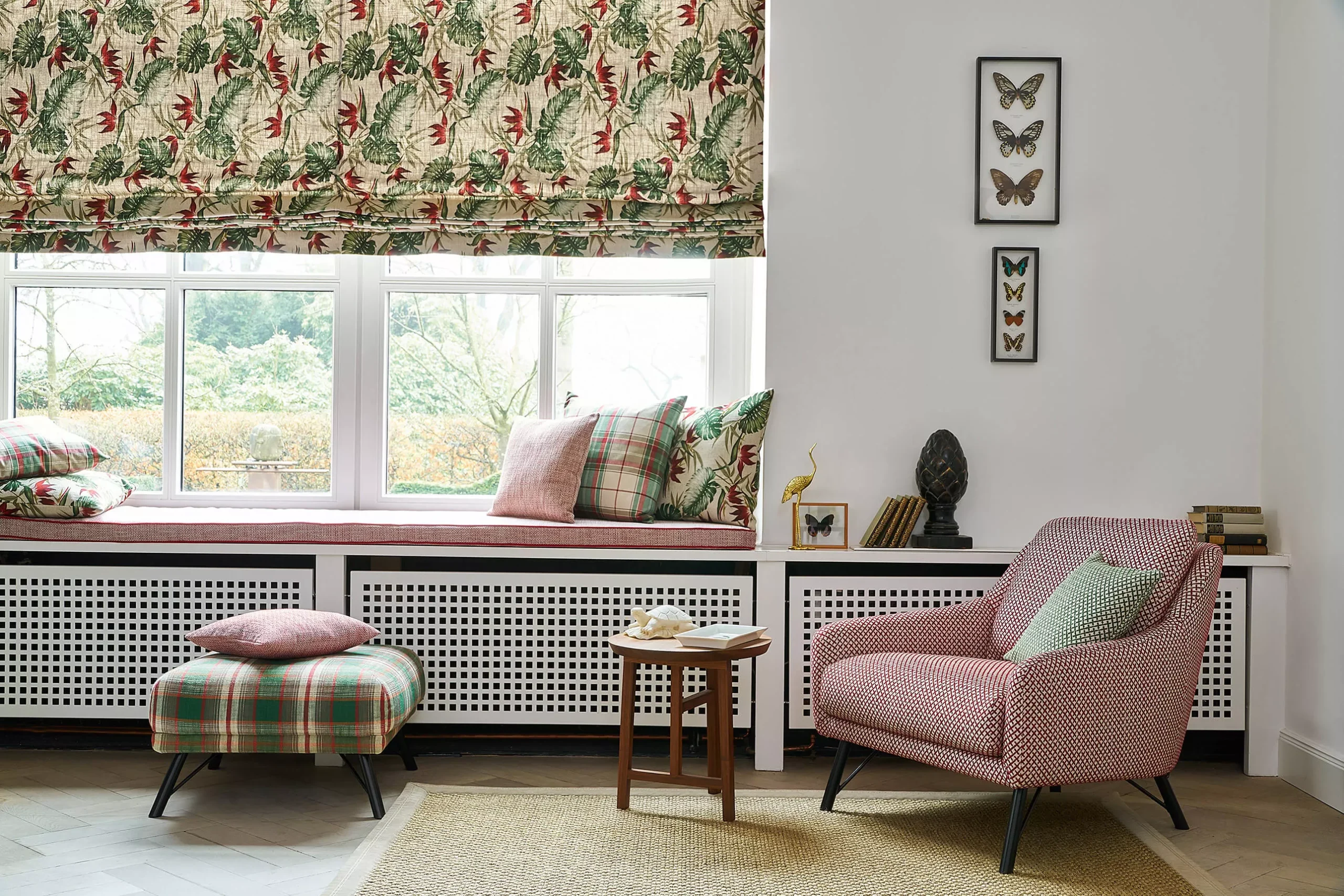 Wohnzimmer mit gemustertem Raffrollo und rosa Sessel.