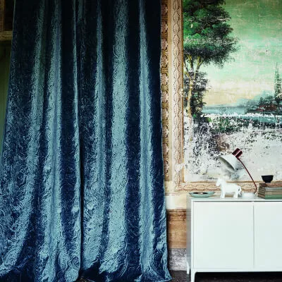 Blau glänzender Vorhang aus Samt mit neben Wand mit Motivtapete sowie Tisch und Lampe