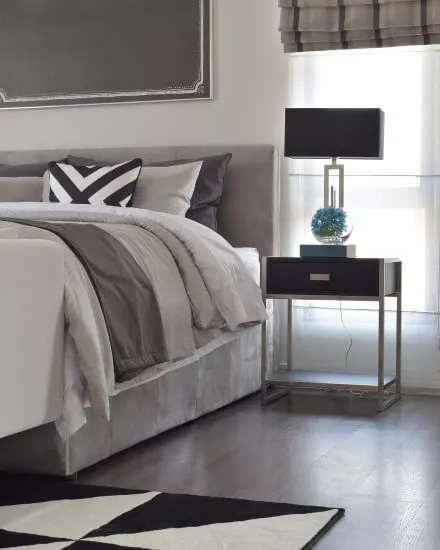 Ein modernes Schlafzimmer mit Raffrollo, Bettbezügen und Kissen in den Farben Grau und Beige.