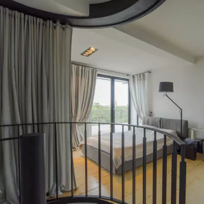 Blick durch ein Metallgeländer mit raumteilendem Vorhang in ein Kreativ gestaltetes Schlafzimmer mit Terrassentür und maßgeschneidertem Design.
