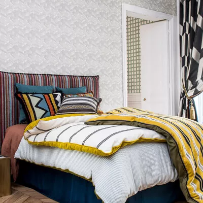 Bett mit Streifenmuster und verschiedenen Decken, gemusterte Tapete und Beistelltisch im Vordergrund