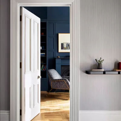 Blick durch eine offene graue Tür auf blaue Einbaumöbel und Sessel, daneben Wand mit grauer strukturierter Tapete und Regal mit Pflanze