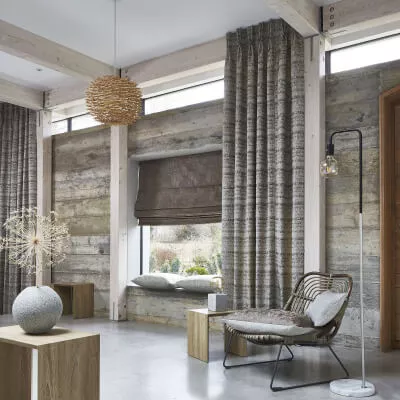 Grau-braun melierte Vorhänge mit Faltenband vor einer Betonwand in einem modernem Wohnzimmer mit braunem Raffrollo.