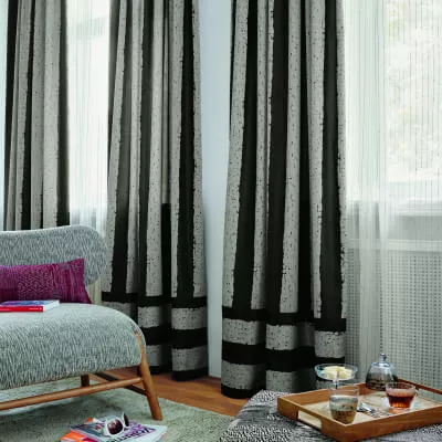 Zwei Fenster mit Vorhängen in Grautönen und einem Sofa