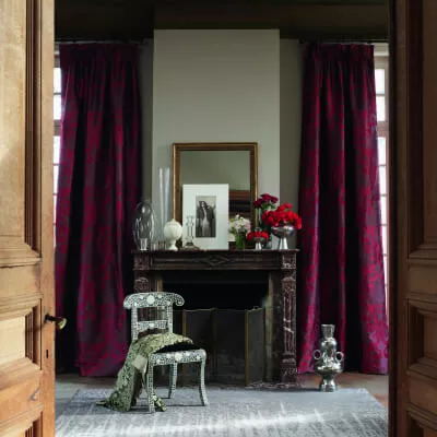 Schwere rote Vorhangschals mit Ornamenten hängen in einem klassischen Ambiente mit Kamin.