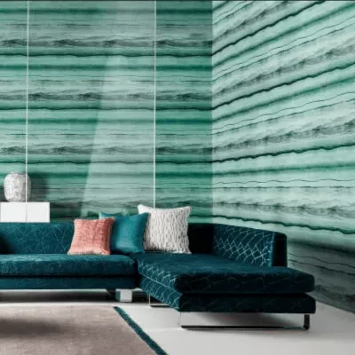Ein Wohnzimmer mit grün gemusterten Tapeten über Eck sowie Couch mit Kissen