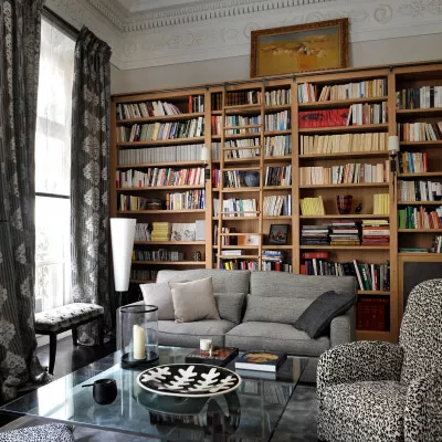 Altbauzimmer mit vollgepacktem Bücherregal,schwarz-weißen Vorhängen und Sofa.